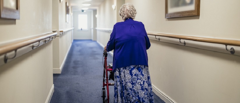 care home resident walking down corridor with zimmer frame, social care