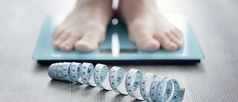 person stood on scales with tape measure in front, obesity