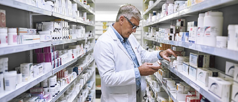 pharmacist standing is aisle with medicines, pharmacy