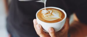 barista pouring milk into cup of coffee