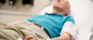 A senior man is lying down on a hospital bed while taking pulse oximetry