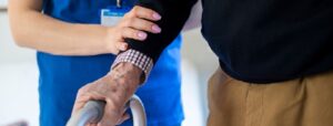 nurse helping older man walk with zimmer frame in social care setting