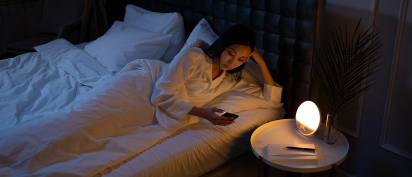 woman lying in bed looking at phone, insomnia, sleep, sight loss