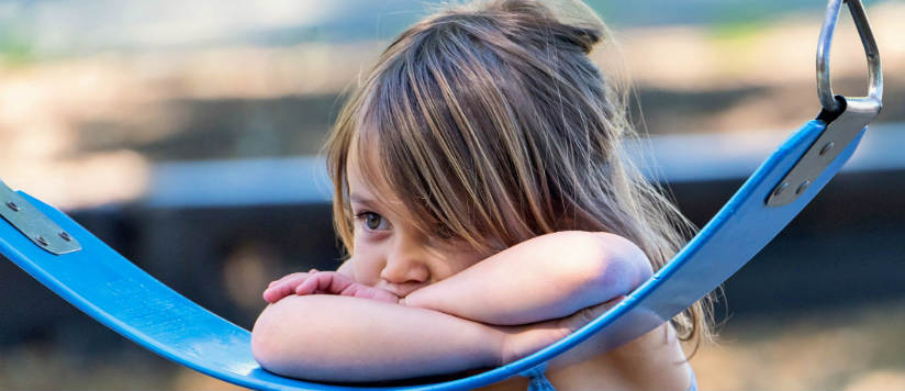 Child looking sad leaning on a swing