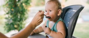 Baby eating solid food in high chair, weaning