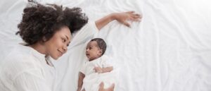 Closeup portrait of beautiful young African American mother day girl kiss healthy newborn baby sleep in bed flat lay copy space.