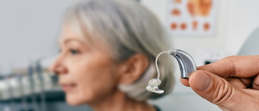 Close-up of hearing aid near senior patient's ear at audiology clinic. Hearing solutions, hearing BTE aids