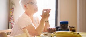 Senior woman eating breakfast early morning, back lit and with a sad expression. She is wearing her nightgown.