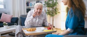 Elderly woman retirement home patient eating meal that young nurse brought to her