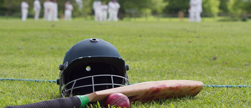 Cricket helmet, bat and ball on boundary line during a game in the English village.