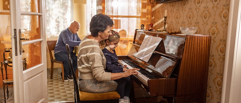 Mature woman teaching her little niece how to play a piano in her home.